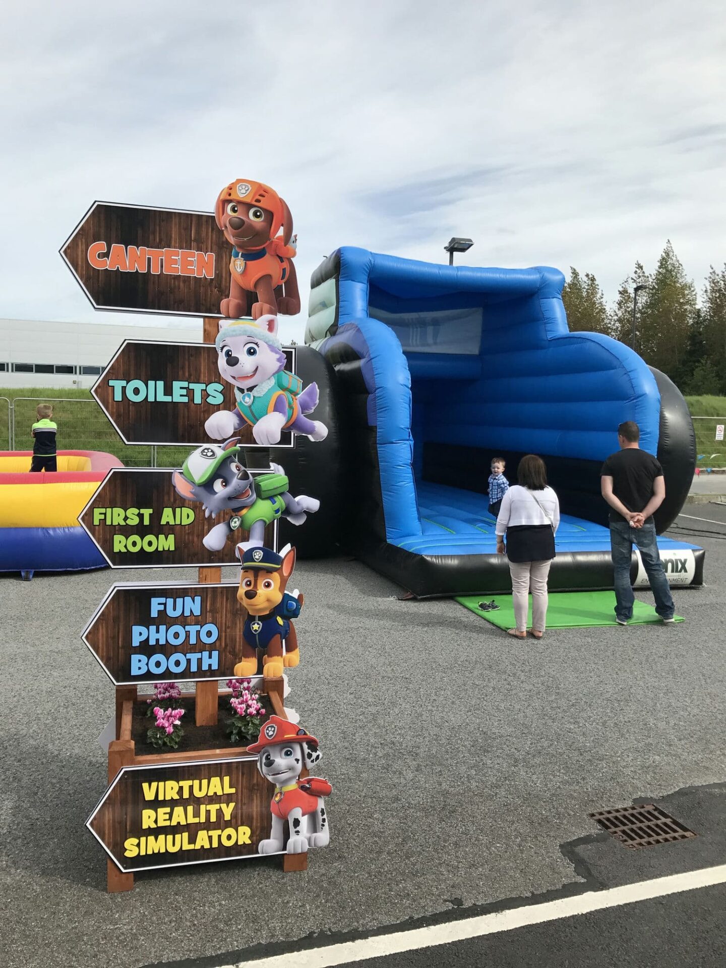 A sign post printed with Paw Patrol characters and a large inflatable bouncy castle at an outdoor kids party in Dublin