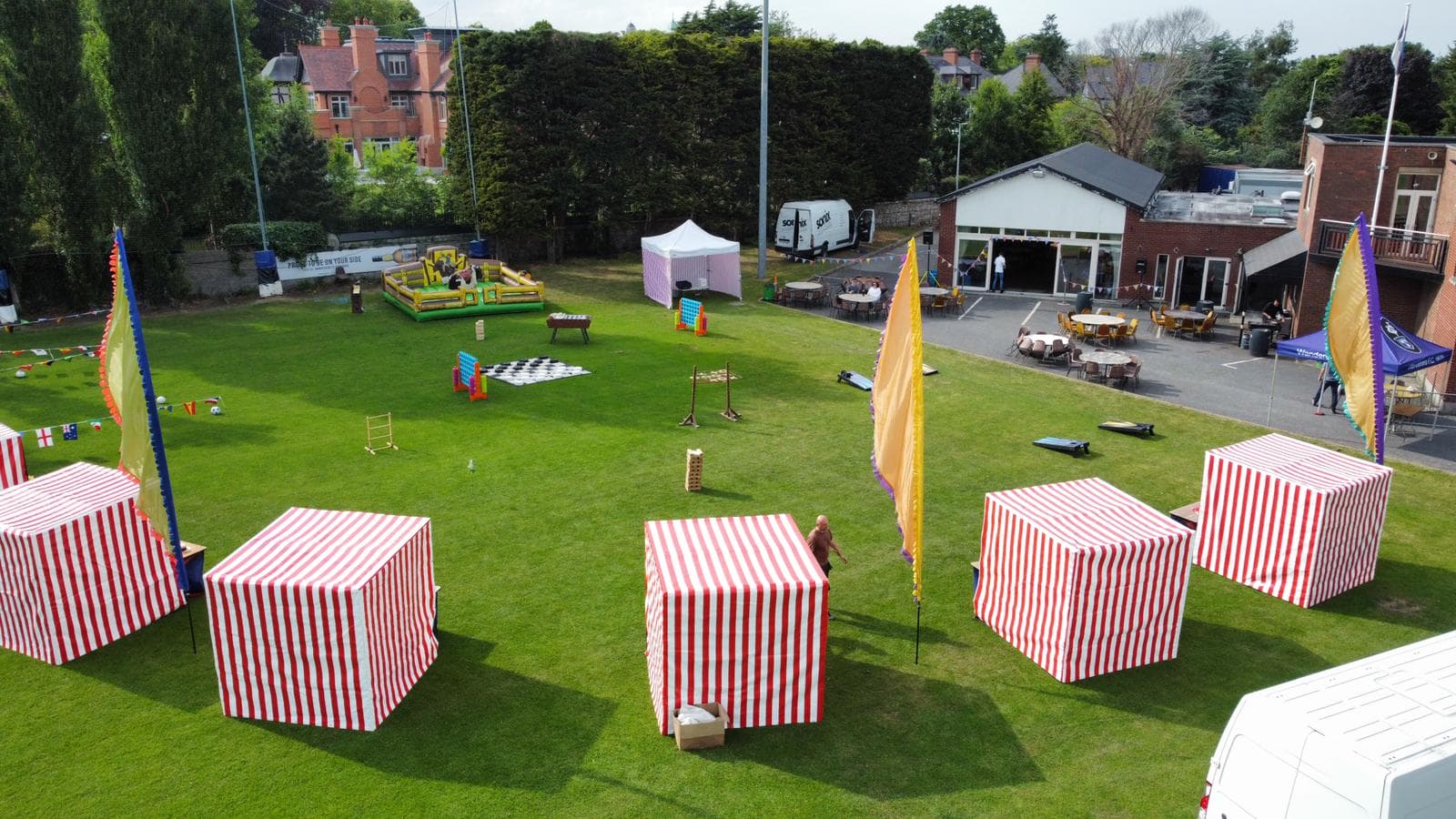 An assortment of games stalls are arranged on a grassy field outside an Irish hotel for a company summer party