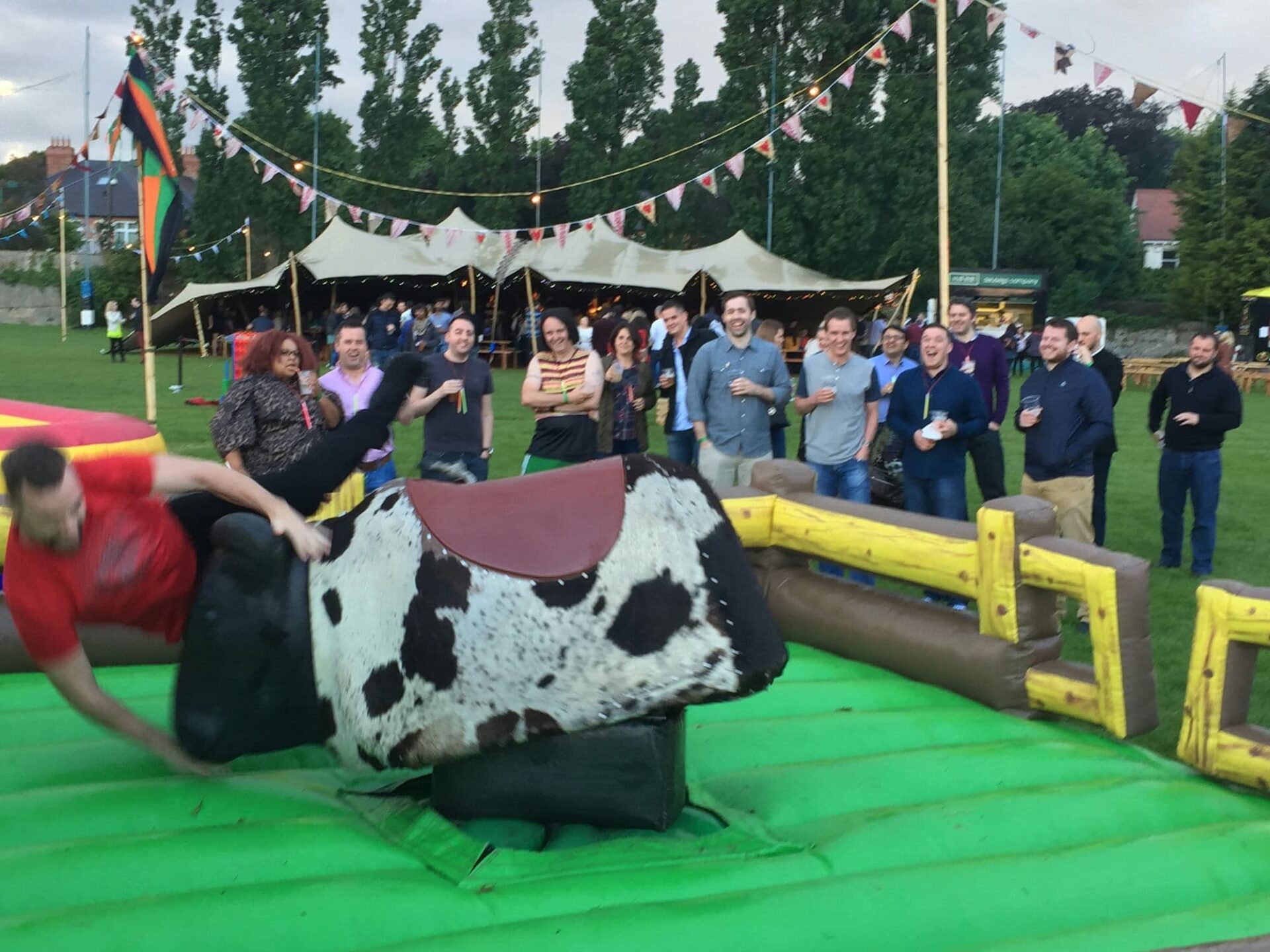 a group of guests enjoy watching one of their group thrown off a bucking bronco mechanical bull ride at an outdoor corporate work party in Dublin