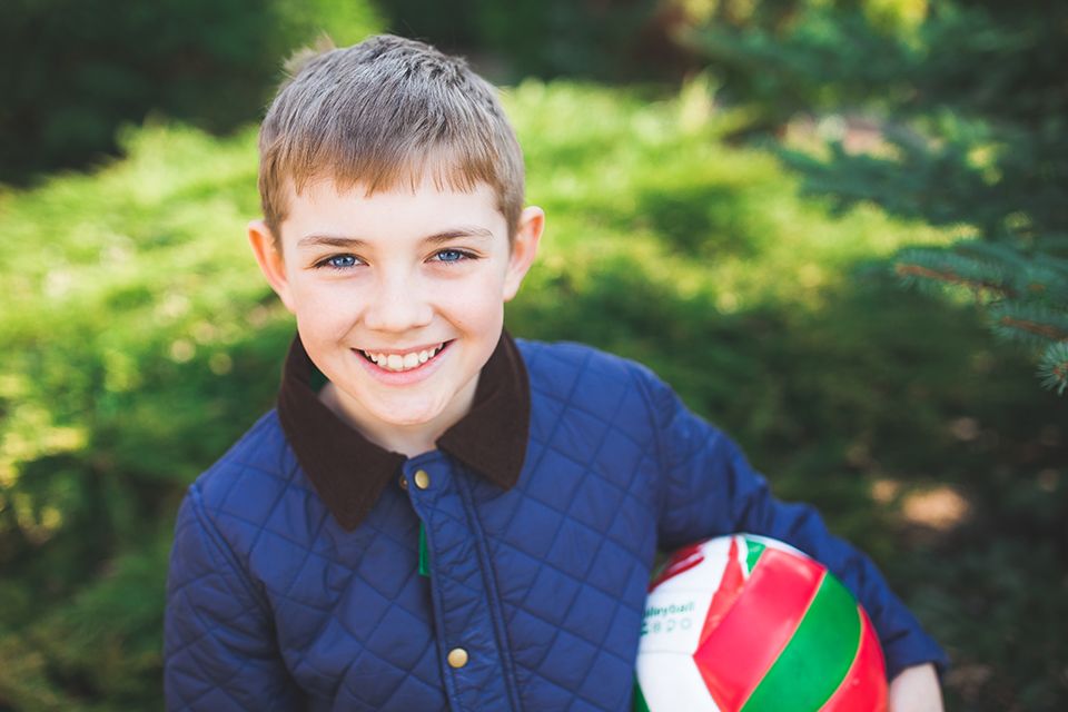 young boy holds a ball and smiles at an outdoor summer event